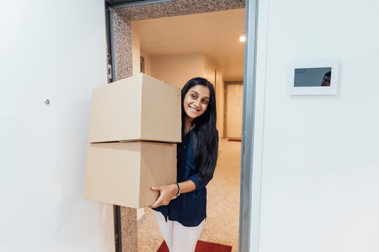 Smiling woman holding boxes walking in home