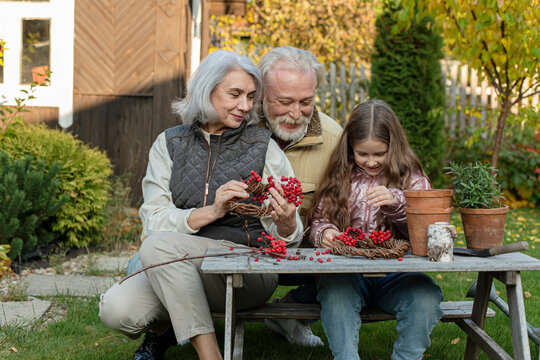 Grandparents and granddaughter sitting at garden table crafting with mountain ash