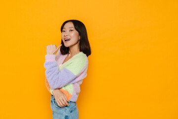 Young asian girl pointing away with thumb isolated over yellow background