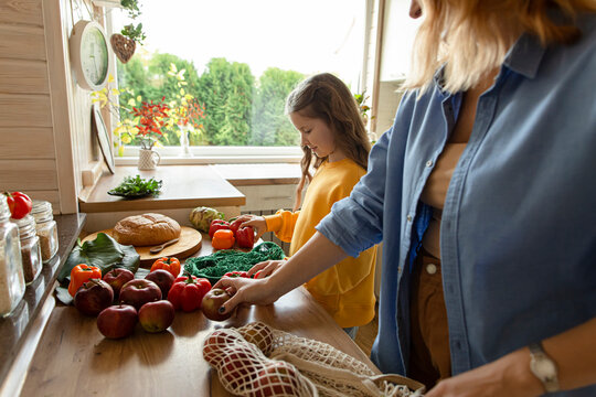 Mother and daughter unpacking fresh groceries in kitchen - Powered by Adobe