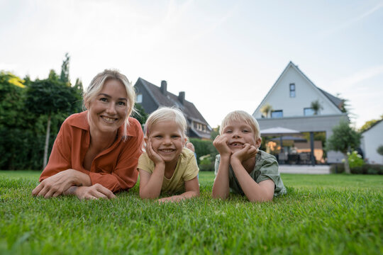 Smiling woman with children leaning on elbows in back yard