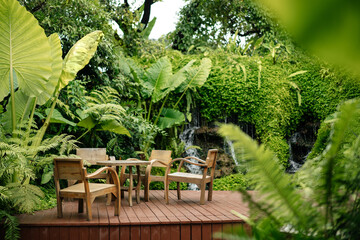 Wooden chairs and tables on the street in the tropics among the foliage. Exterior of cafe or lounge...