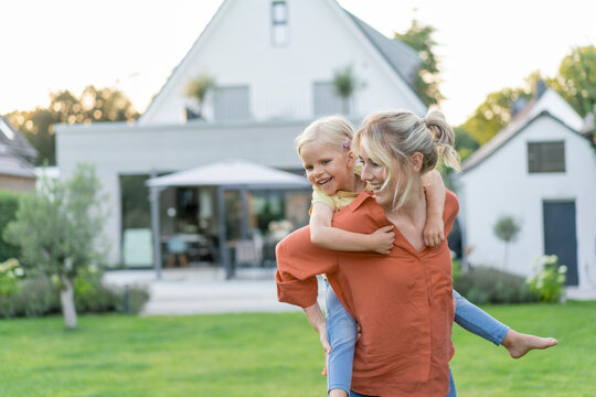 Happy mother giving piggyback ride to daughter in garden