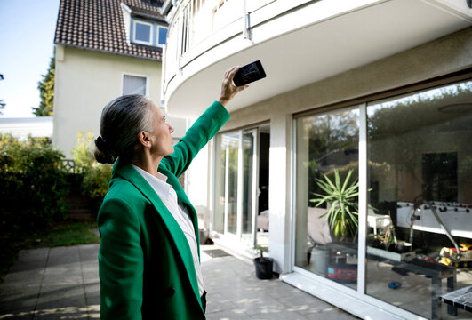 Senior businesswoman photographing house through smart phone