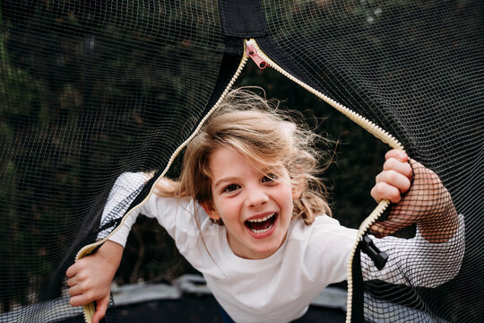 Happy girl looking through net on trampoline in garden