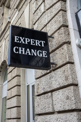 Obraz premium Black sign of a money exchange office with the words ' Expert change ' in white on a gray brick wall. Billboard for a professional place to exchange money.