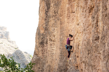 The girl climbs the rock. The climber is training to climb the rock. A strong athlete overcomes a difficult climbing route. Extreme hobby. A woman goes in for sports in nature.