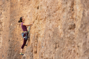 The girl climbs the rock. The climber is training to climb the rock. A strong athlete overcomes a difficult climbing route. Extreme hobby. A woman goes in for sports in nature.