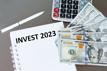 Invest 2023 text on a notebook on the table next to the calculator and dollar bills