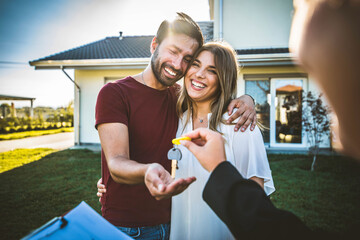 Happy millennial couple receiving keys from realtor, purchasing real estate - Family meeting with...