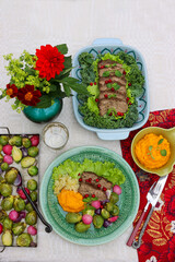 Colorful nutritious food, beautifully presented with red flowers. A green plate filled with liver pate, pumpkin puree, sauerkraut and Brussels sprouts. Good and healthy paleo food for a nice Christmas