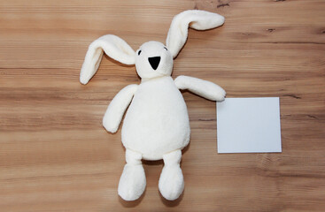 children's toy a white hare with long ears holds a white greeting card in its paws, close-up on a...