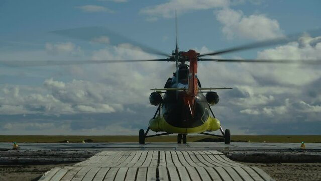 Helicopter preparing for takeoff, propellers rotate. Mi-8 helicopter on wood helipad, rear view.