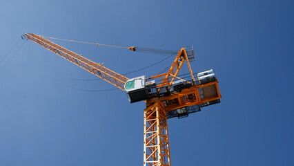 Yellow tower crane luffing boom soars isolated into blue sky