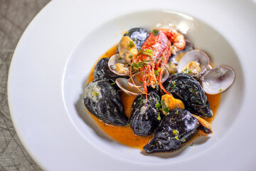 Cuttlefish ink culurgiones (nero di seppia)  with clam sauce and prawns, traditional pasta from Sardinia, Italy