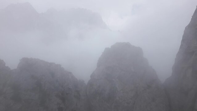 Passing steep rocky ridges and revealing huge mountains in the Alps. Spectacular views in the Dolomites, in thick clouds. Majestic mountain up in the clouds, captured by drone in 4k, 24fps.