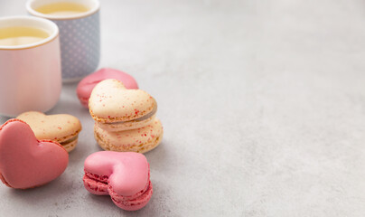 Cake macaron or French macaroon in heart shapes, two cups on grey background with copy space. Colorful almond cookies, pastel colors.