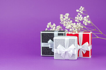 Large and small gift boxes on a purple background with a bouquet of gypsophila