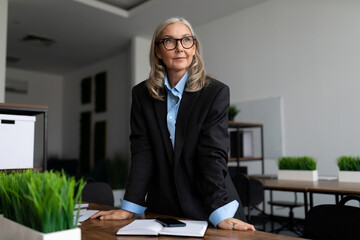 senior businesswoman caucasian stands at the desk and looks at the camera