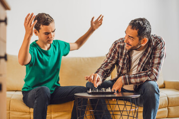 Father and son are playing chess at home. Boy is angry because he is loosing.