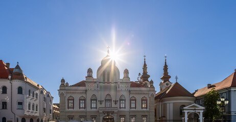 Obraz premium Setting sun rays shine brightly above facade roof of diocese (eparchy) of Serbian Orthodox Church (Episcopia Ortodoxa Sarba) on central Union Square (Piata Unirii) in Timisoara, Romania