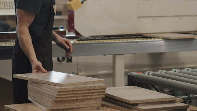 Tilt up shot of man putting boards from conveyor belt into wood finishing machine while working at furniture factory