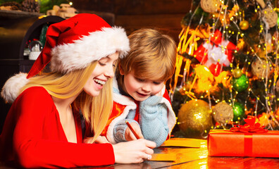 Mom and kid write wishlist to santa.play together christmas eve. Mother and little child boy having fun. Family having fun at home christmas tree