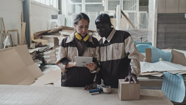 Caucasian woman explaining something on tablet to African American colleague while working together in factory warehouse