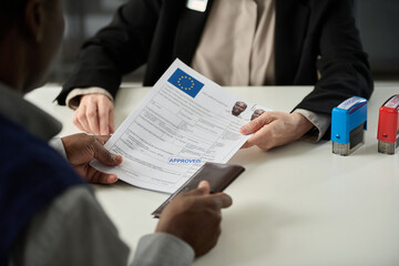 Close up of unrecognizable consulate worker handing approved visa application form to black man in office