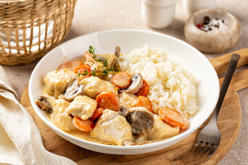 Blanquette de poulet with rice, French chicken stew with carrots, mushrooms, onion. Simmered in a white stock and served in a sauce enriched with cream in a white plate.