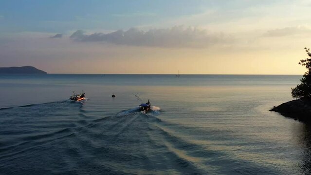 Aerial drone fly around two fishing boats sailing into the ocean to catch fish at sunset golden hour, Langkawi island, Kedah, Malaysia, Southeast Asia.