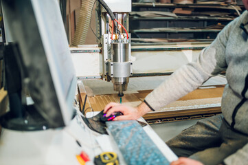 Factory worker operating drilling cnc machine at wood machining industry