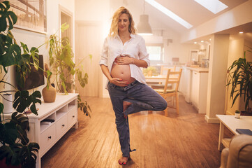 Portrait of pregnant woman standing at home holding hands on her belly