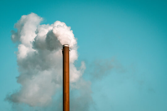 Factory chimney blowing white smoke from pipe in blue sky