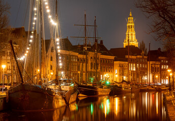 Fototapeta na wymiar Cityscape of Groningen at night, view of historical ships, canal and tower of the Aa-kerk church
