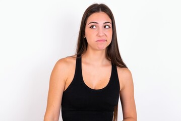 Fototapeta premium Young caucasian woman wearing sportswear over white background has worried face looking up lips together, being upset thinking about something important, keeps hands down.