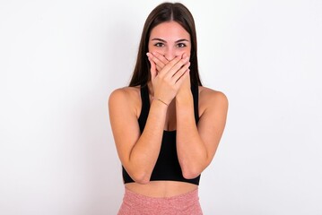 Fototapeta premium Upset Young caucasian woman wearing sportswear over white background , covering her mouth with both palms to prevent screaming sound, after seeing or hearing something bad.
