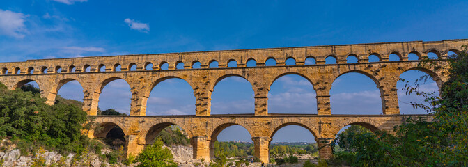 Panorama view to the limestone Pont du Gard three-tiered aqueduct at the river Gardon.