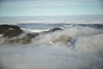 Above sea of fog in winter mountains. Sunny day in snow covered Carpathian Mountains. Clouds above clear sky