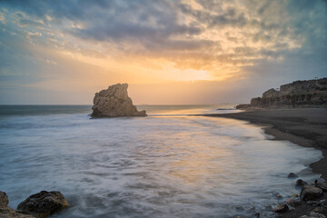 Sunset on the beach of Pe on del Cuervo in Malaga. The sun sets on the horizon between the rocks with an orange sky.