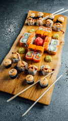 A Vertical closeup of set of sushi rolls with chopsticks on the wooden board, party food. Fresh food..