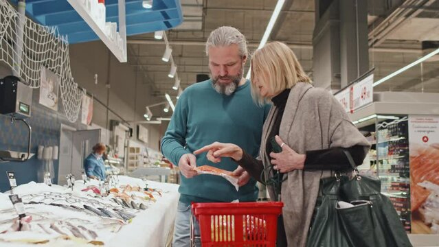Caucasian mid adult couple choosing and buying fish while food shopping in supermarket on weekends