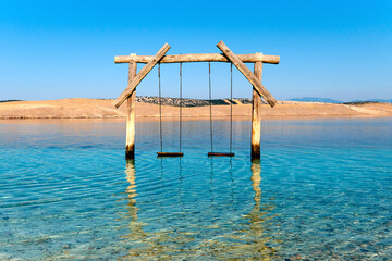 Empty swing in the water. Pebble beach on Adriatic coast of Croatia. Island Krk on background....