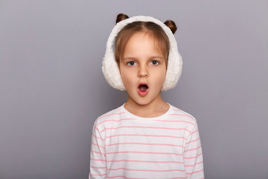 Indoor Shot Of Shocked Amazed Surprised Little Girl Standing And Looking At Camera With Open Mouth, Sees Something Astonishing, Hearing Breaking News.