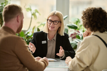 Portrait of female insurance broker consulting couple in agency and smiling explaining application...