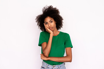 Fototapeta na wymiar Portrait of bored young woman leaning head on hand over white background. African American lady wearing green T-shirt and jeans looking at camera with indifference. Boredom and exhaustion concept