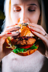 young woman eating burger in hands on black background