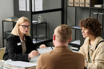 Portrait of mature female insurance broker consulting couple in office and holding application forms