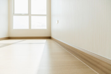 Empty room closeup on an engineering wooden floor and baseboard with sunlight from the window. Minimalist interior design and real estate for decoration. Real image with copy space.