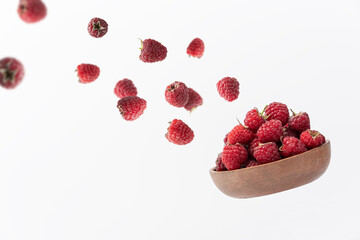 Wooden bowl with raspberries and berries flying in the air on white background. Food levitation...